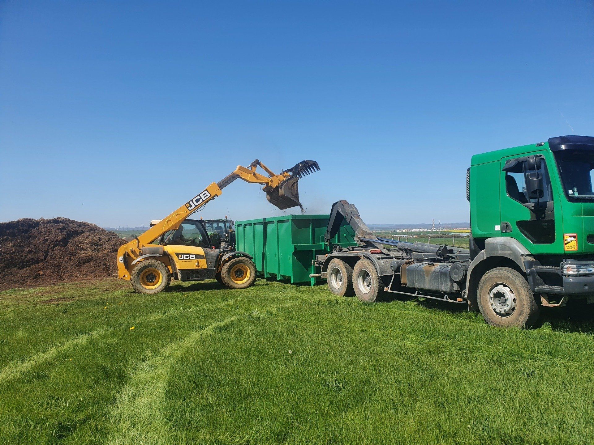 Chargement d'une benne verte avec une minipelle jaune