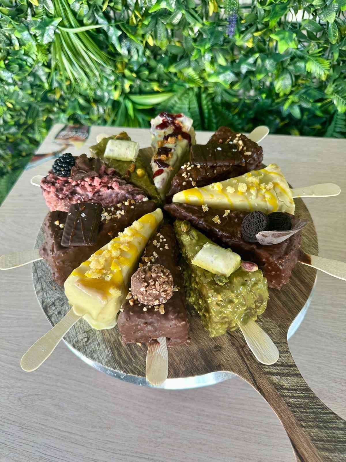 Varias rebanadas de pastel en palitos de madera dispuestos sobre una tabla de madera sobre un fondo verde.