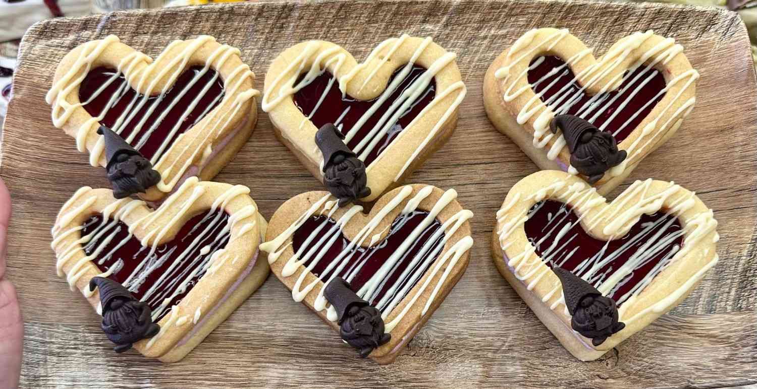 Seis galletas con forma de corazón con relleno de mermelada, glaseado blanco y detalles.