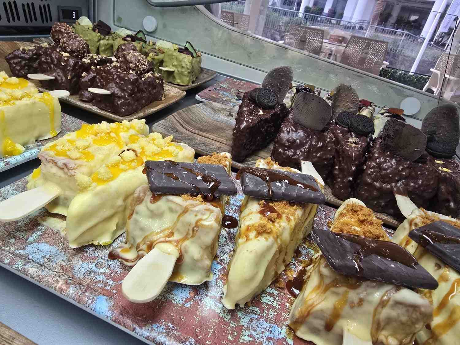 Vitrina con diversos postres en forma de paleta, cubiertos de chocolate y aderezados con salsas y coberturas.