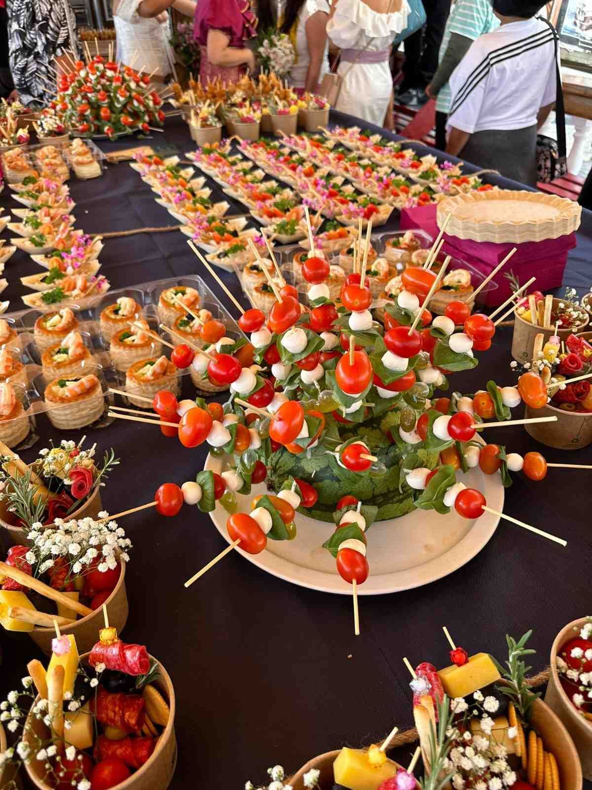 Mesa de comida dispuesta con brochetas, tomates, mozzarella y otros aperitivos, para un evento.