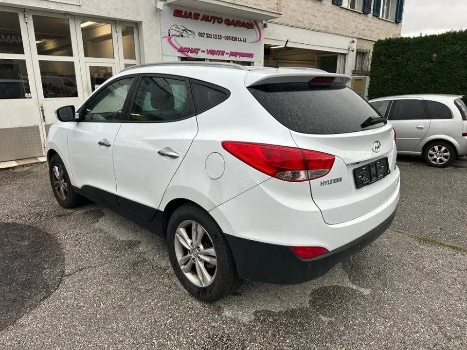 Un SUV Hyundai ix35 blanc est garé dans un garage automobile, une autre voiture étant visible en arrière-plan.