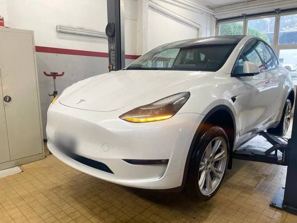 Une Tesla Model Y blanche garée sur un pont élévateur hydraulique à l'intérieur d'un atelier de réparation automobile.
