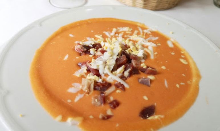 Un plato blanco cubierto con una sopa roja con huevos y tocino.