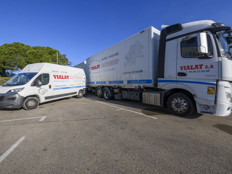 Deux camions de livraison blancs avec des logos rouges étaient garés le long d'une route bordée d'arbres par une journée ensoleillée.
