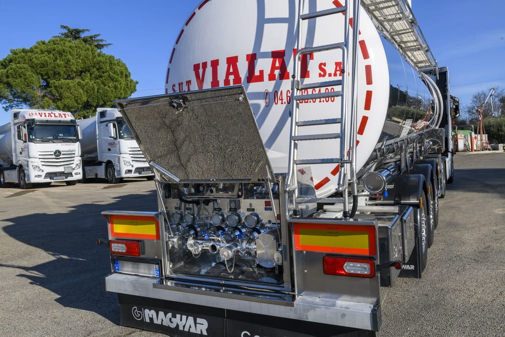 Des camions-citernes à carburant alignés sur un parking, avec un camion-citerne argenté et une échelle au premier plan.