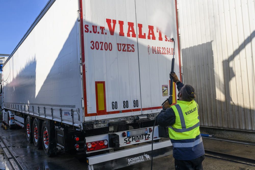 Un ouvrier en gilet jaune ouvre l'arrière d'un camion-remorque blanc.