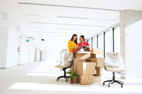 Deux personnes emballent des cartons dans un espace de bureau lumineux et vide.