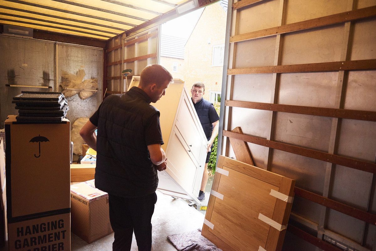 Des hommes déchargent une armoire d'un camion de déménagement, avec des cartons empilés à proximité.