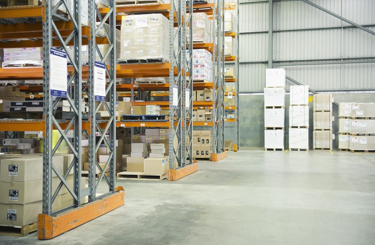 Allée d'entrepôt avec des palettes et des cartons empilés sur des rayonnages métalliques.
