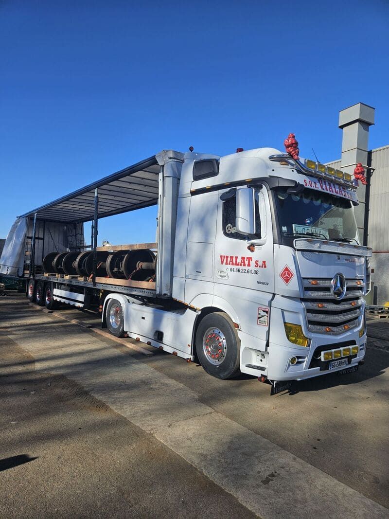Camion porte-voitures blanc stationné sur une route ensoleillée, chargé de plusieurs véhicules