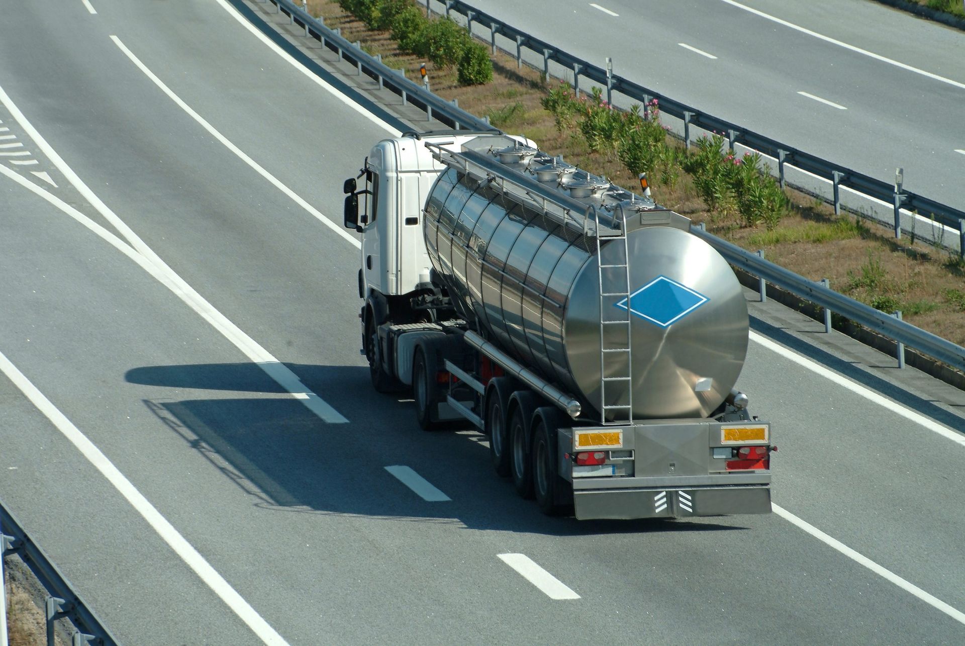 Camion-citerne argenté circulant sur une autoroute, vu du ciel.