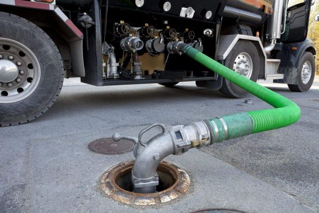 Le tuyau d'un camion-citerne aspire l'eau d'une bouche d'égout dans une rue.