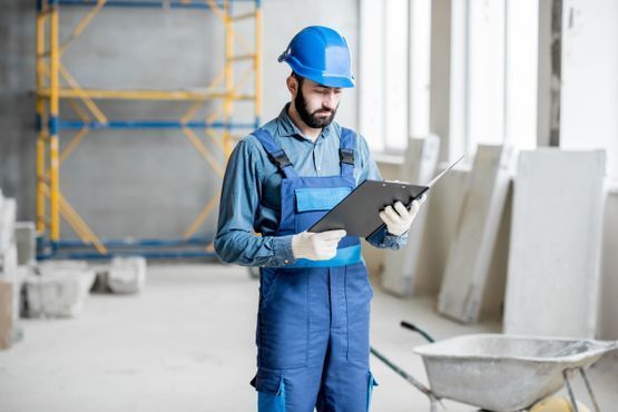 Un trabajador de la construcción está mirando un portapapeles en un edificio en construcción.