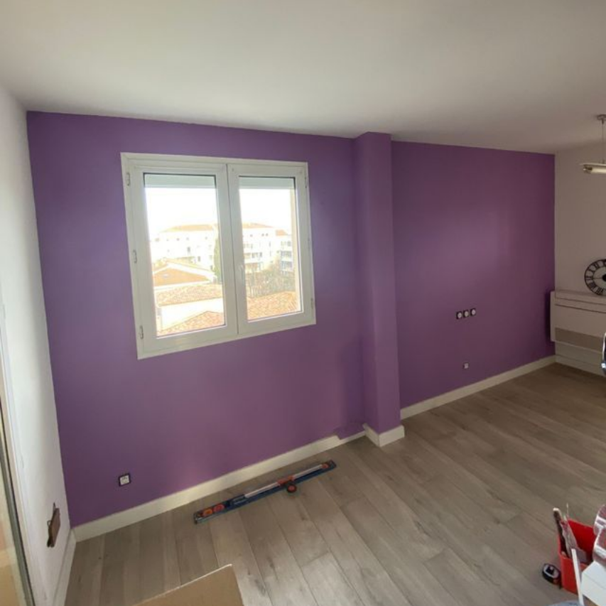 Une main utilise un rouleau à peinture bleu pour appliquer de la peinture blanche sur un mur vierge.