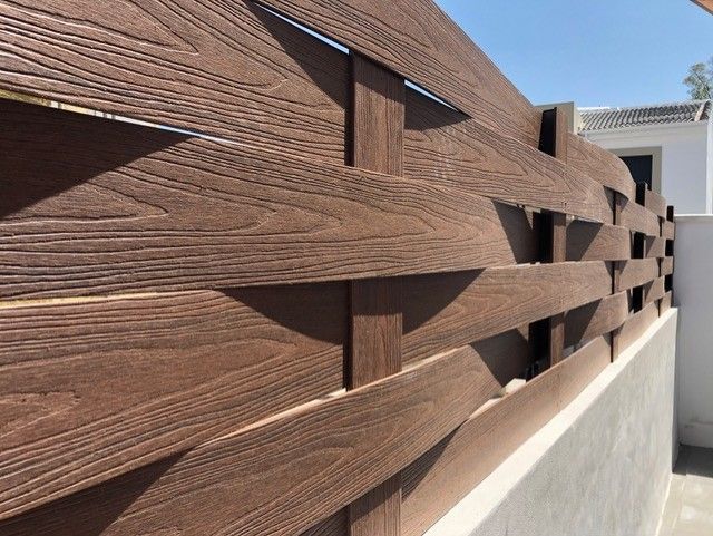 Un primer plano de una valla de madera con un edificio blanco al fondo.