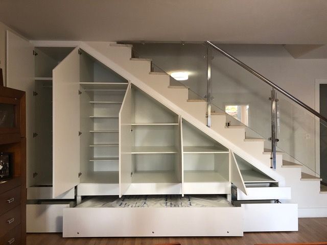 Una escalera con estantes debajo y una barandilla de vidrio.