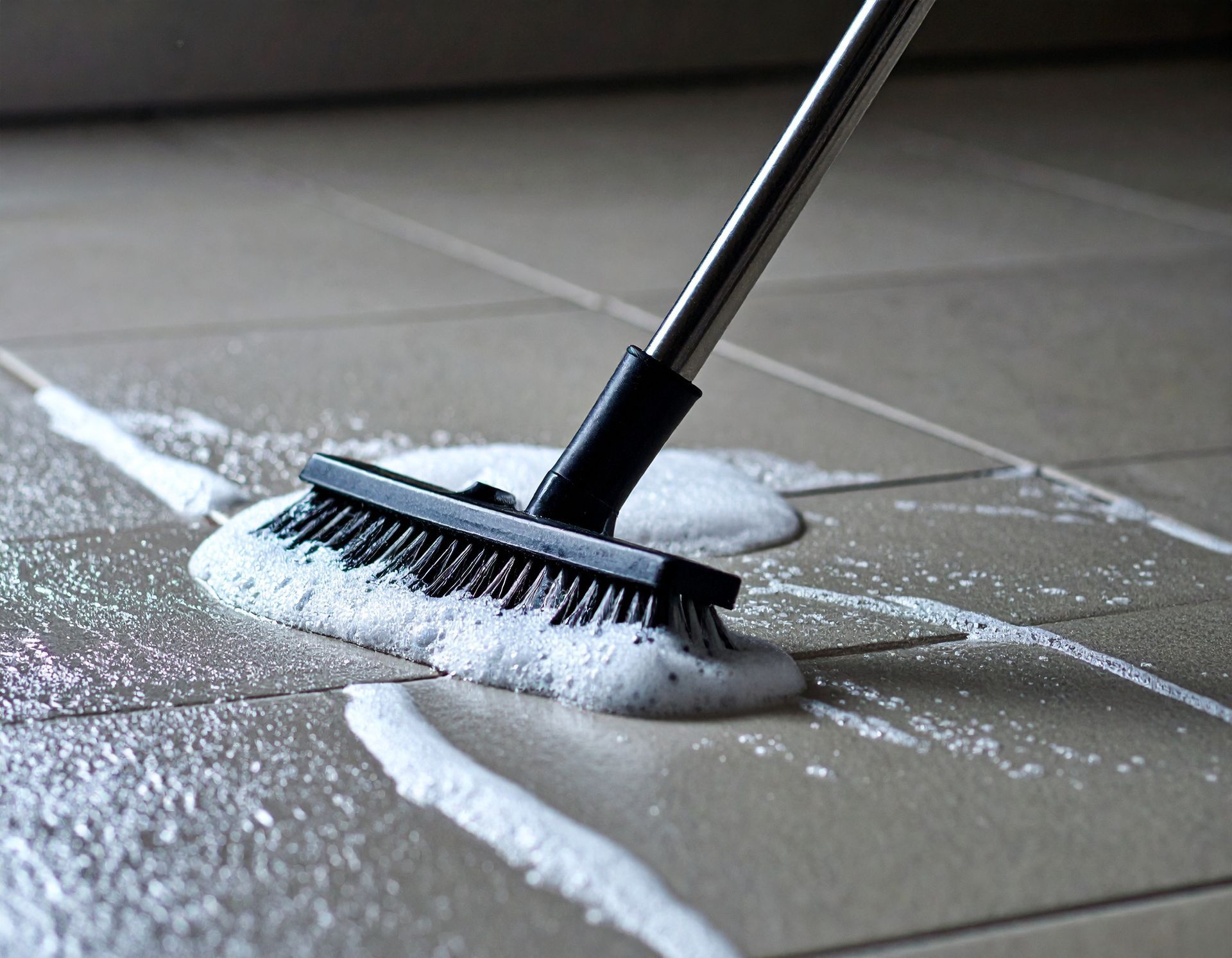 Ein Besen reinigt einen Fliesenboden mit Seife.