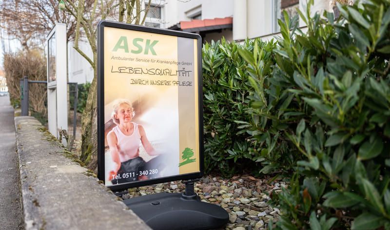 Auf einem Bürgersteig neben einem Busch steht ein Schild mit der Aufschrift „Fragen“.