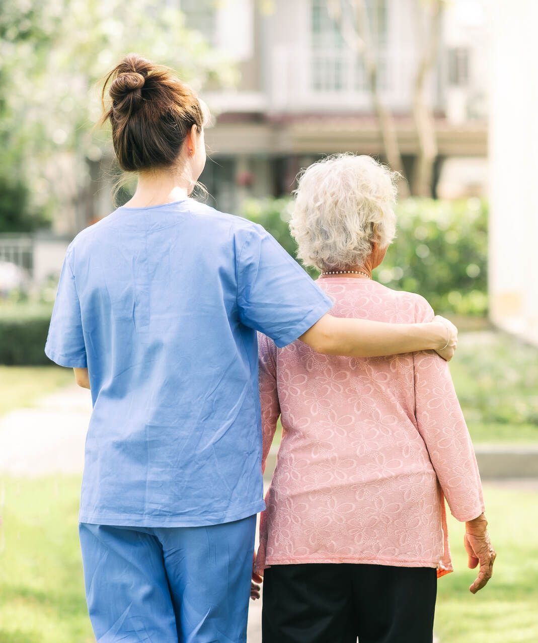 Eine Krankenschwester geht mit einer älteren Frau spazieren.