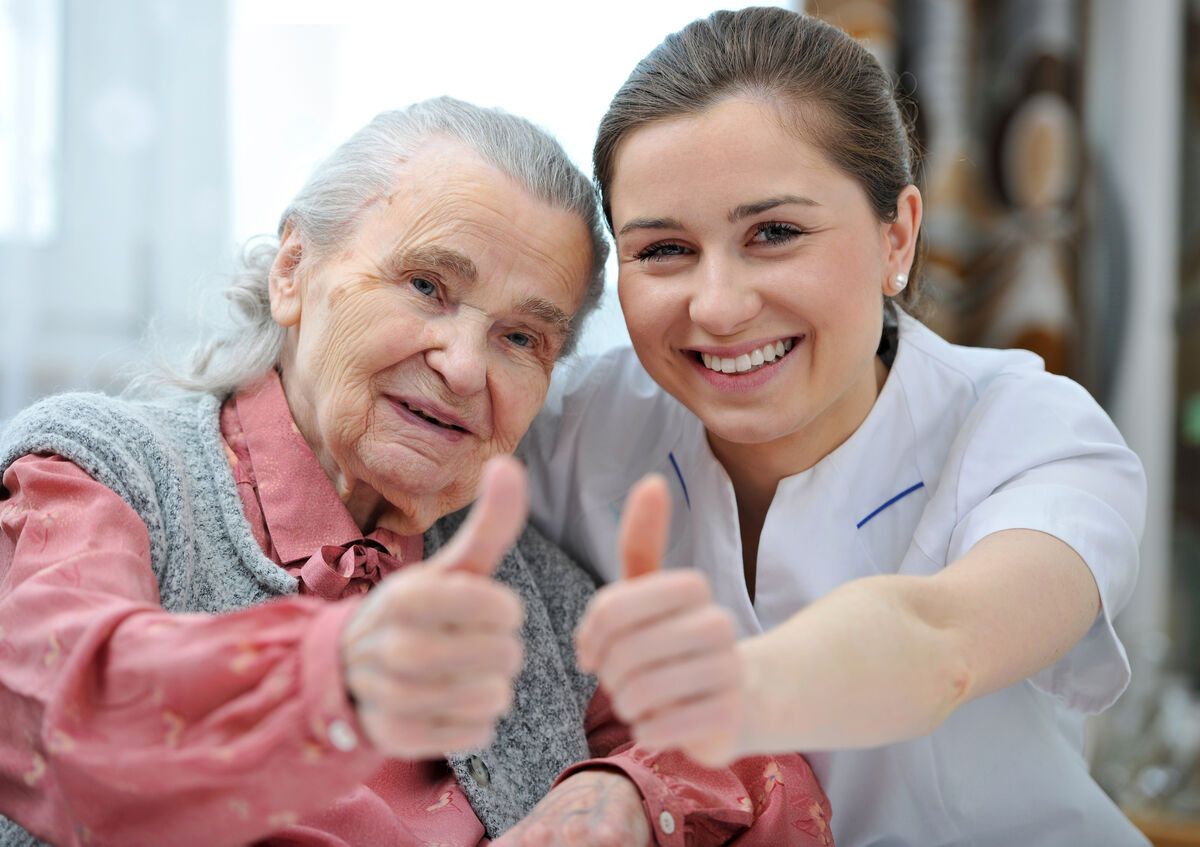 Eine ältere Frau und eine Krankenschwester zeigen den Daumen nach oben.
