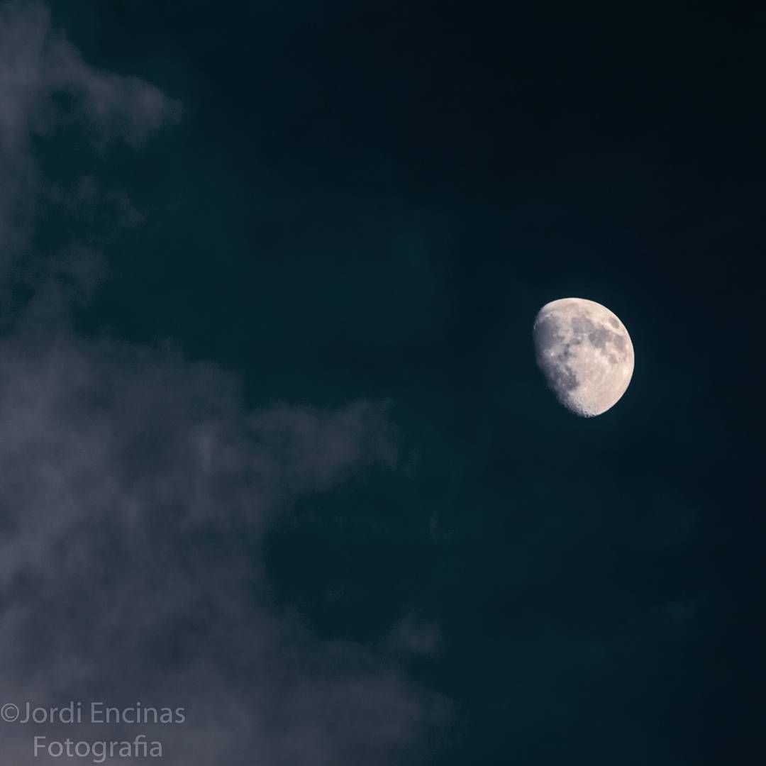 Una media luna es visible en el cielo nocturno rodeada de nubes.