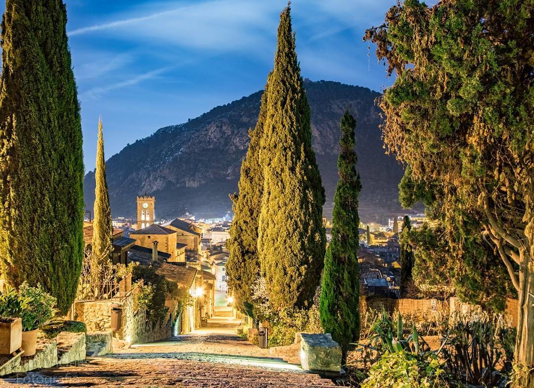 Un camino rodeado de árboles que conduce a una ciudad de noche con una montaña al fondo.
