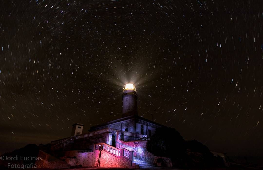 Un faro se ilumina por la noche bajo un cielo estrellado.