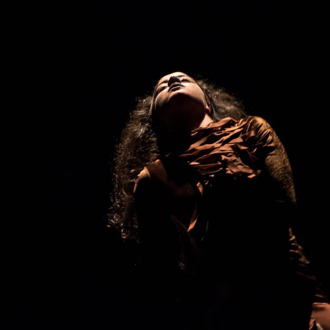 Una mujer está parada en la oscuridad con la cabeza en alto.