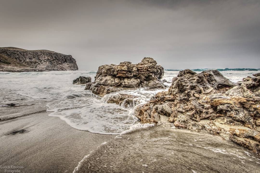 Una playa rocosa con olas rompiendo contra las rocas en un día nublado.