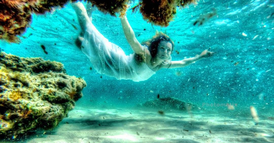 Una mujer con un vestido blanco está nadando bajo el agua en el océano.
