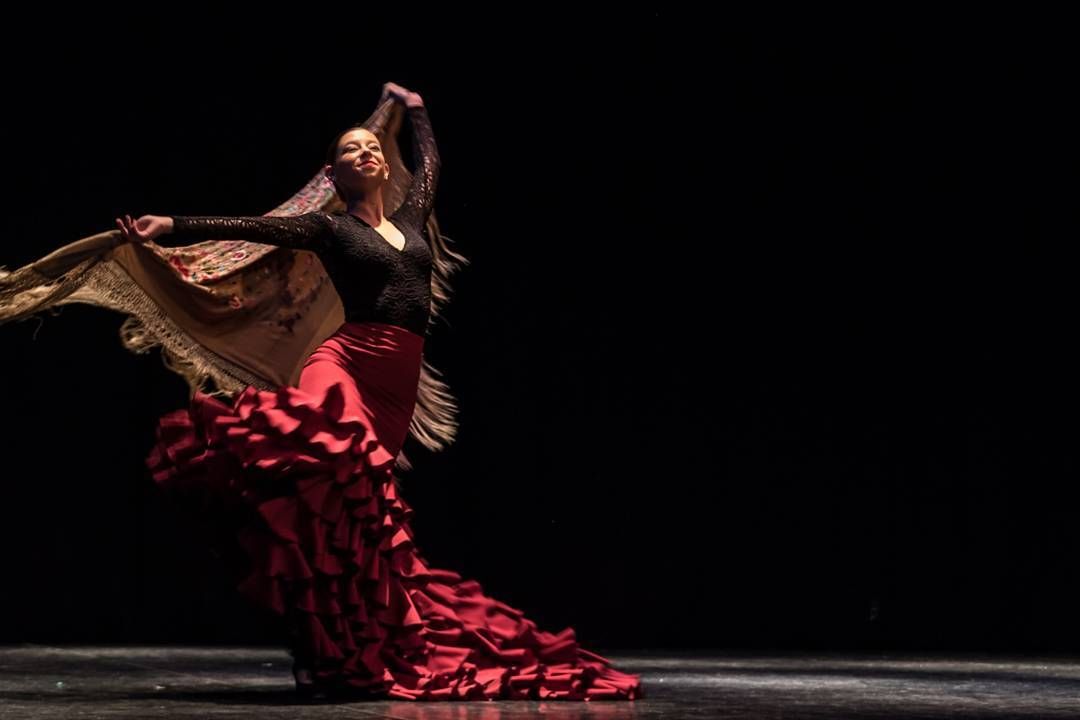 Una mujer con un vestido flamenco rojo está bailando en un escenario.