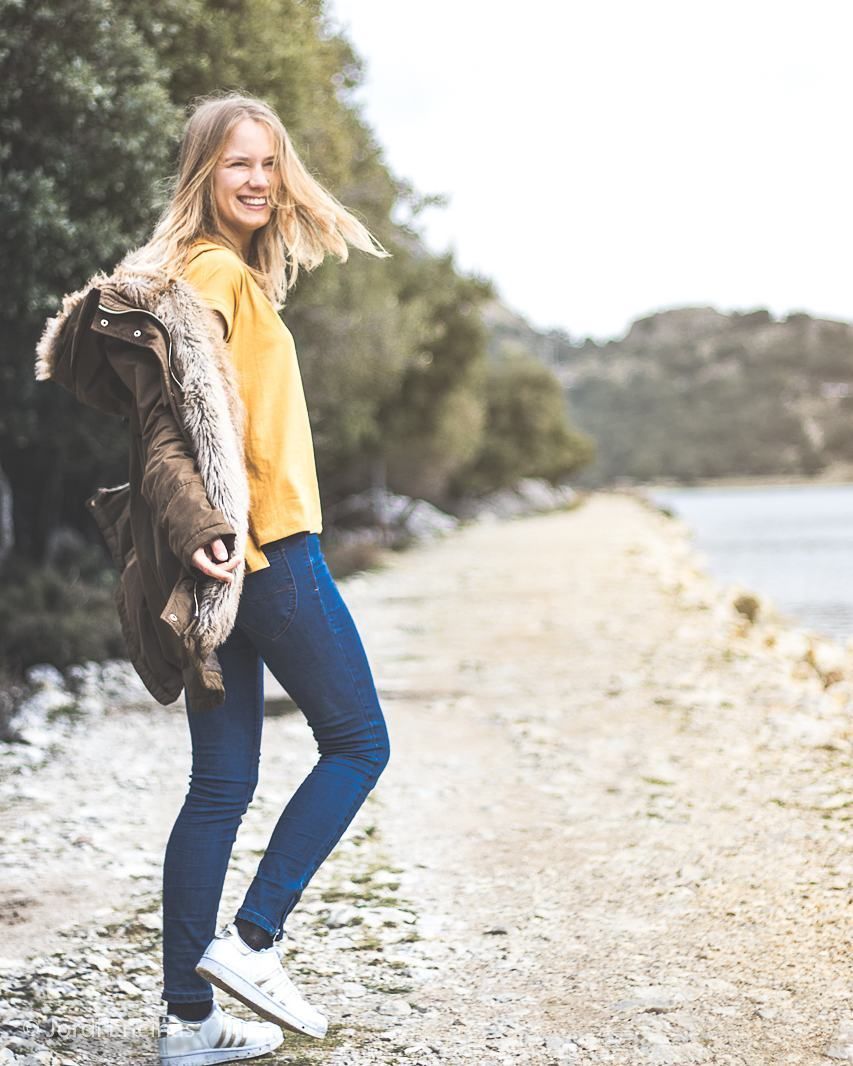 Una mujer con un suéter amarillo y jeans azules está parada en una playa.