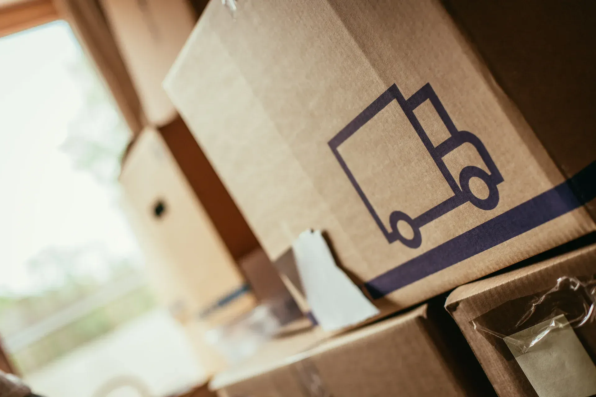 Cajas de cartón para mudanzas, una de ellas con el símbolo de un camión, apiladas cerca de una ventana.