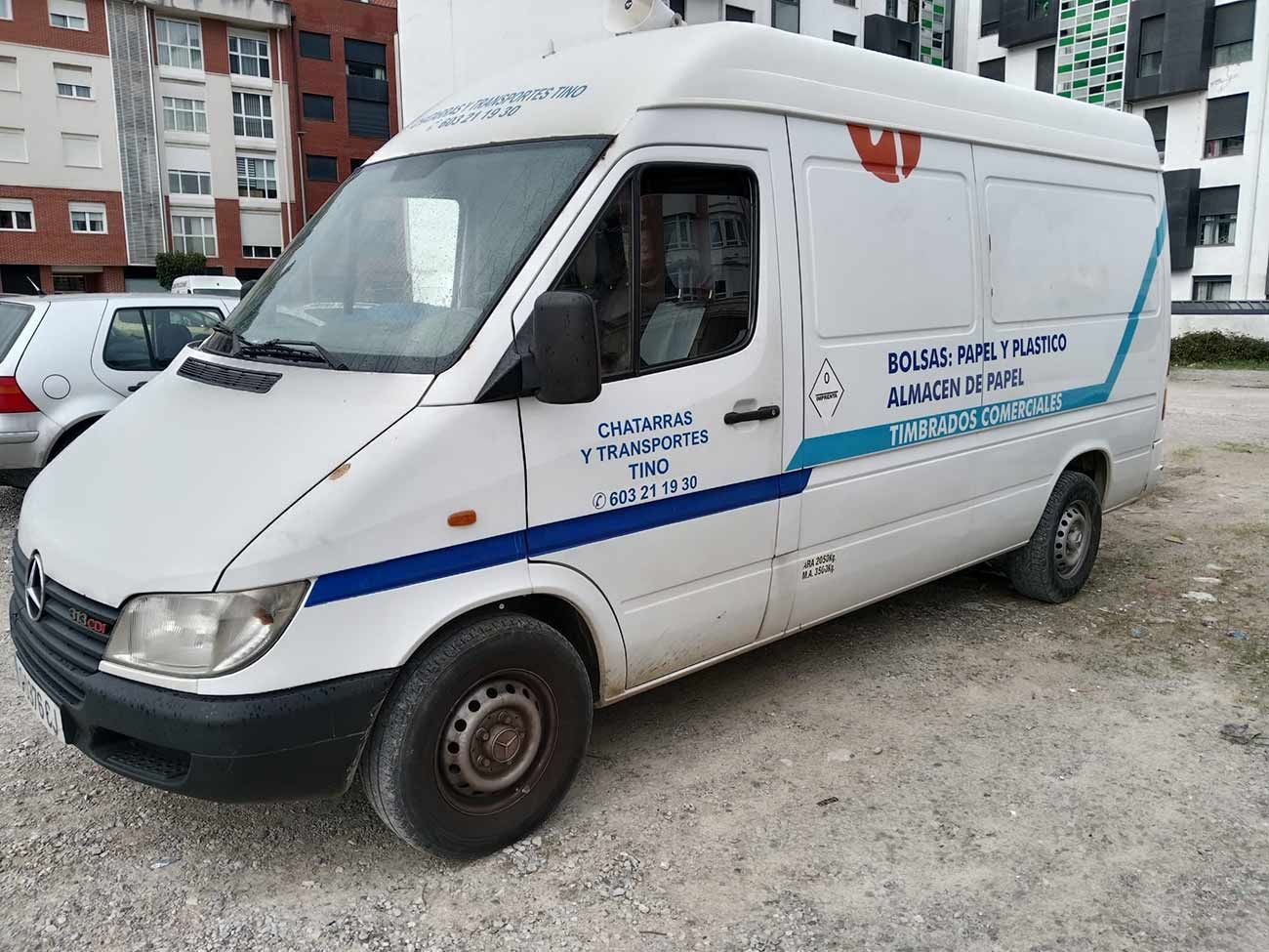 Furgoneta blanca con rayas y texto azules, estacionada al aire libre.