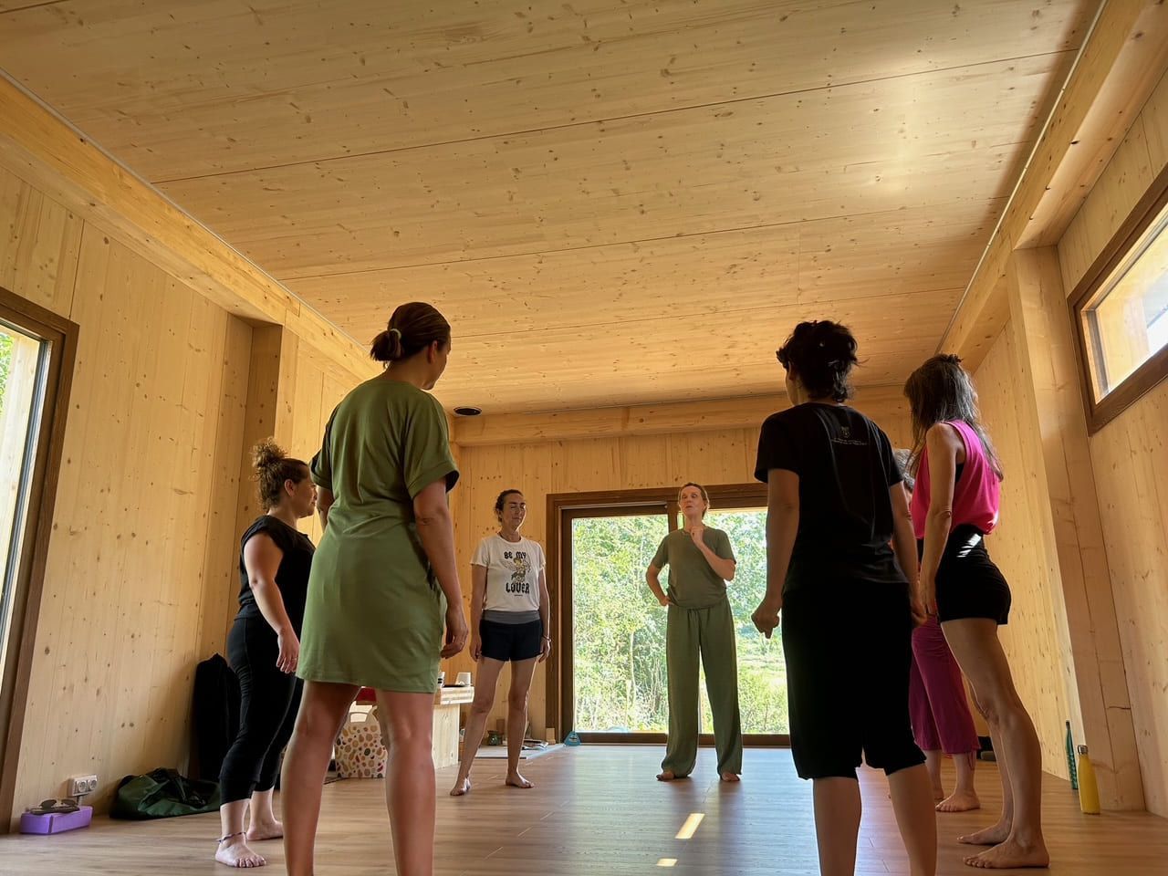 Personas en una sala con paneles de madera clara realizando una actividad grupal. La luz natural entra a raudales por la puerta y las ventanas.