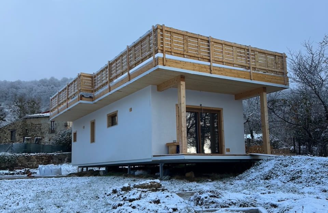 Cabaña blanca con balcón de madera sobre suelo nevado.