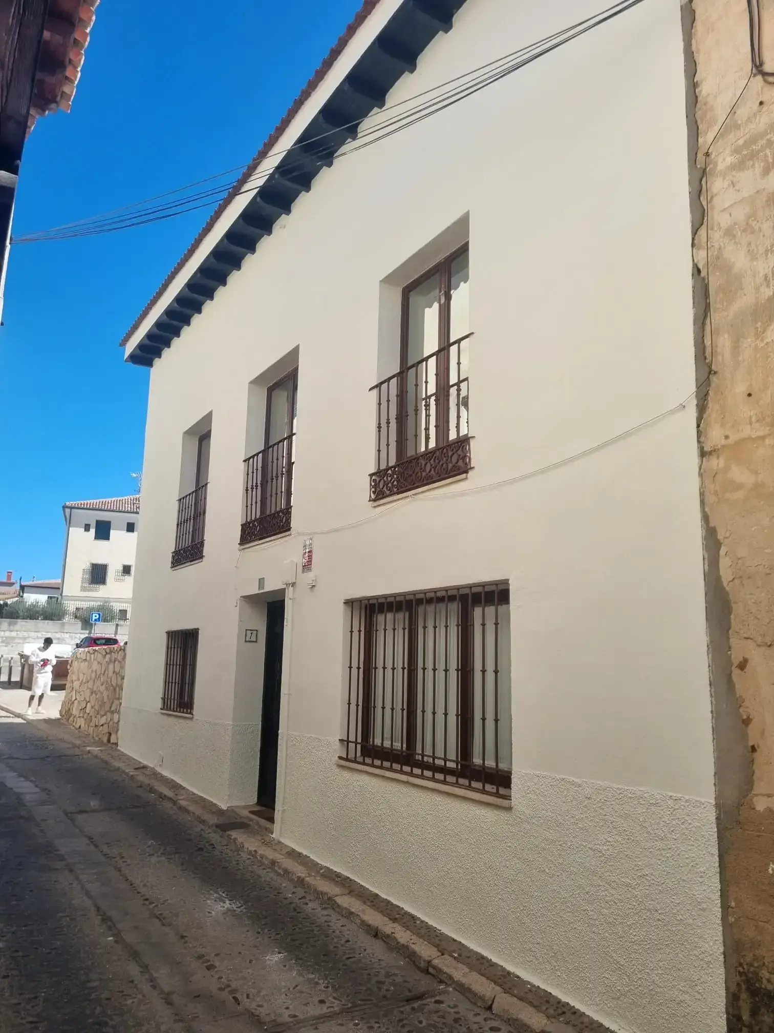 Un edificio blanco de dos pisos, con ventanas de marcos oscuros y un balcón