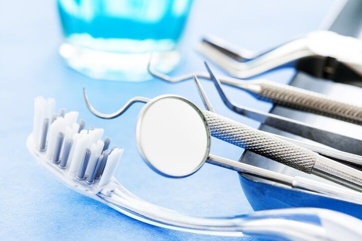 Instrumentos odontológicos e escova de dentes sobre uma superfície azul, com enxaguante bucal azul ao fundo.
