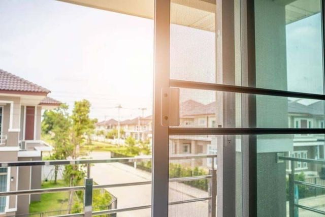 Vista desde el balcón de un soleado barrio residencial a través de puertas corredizas de cristal.