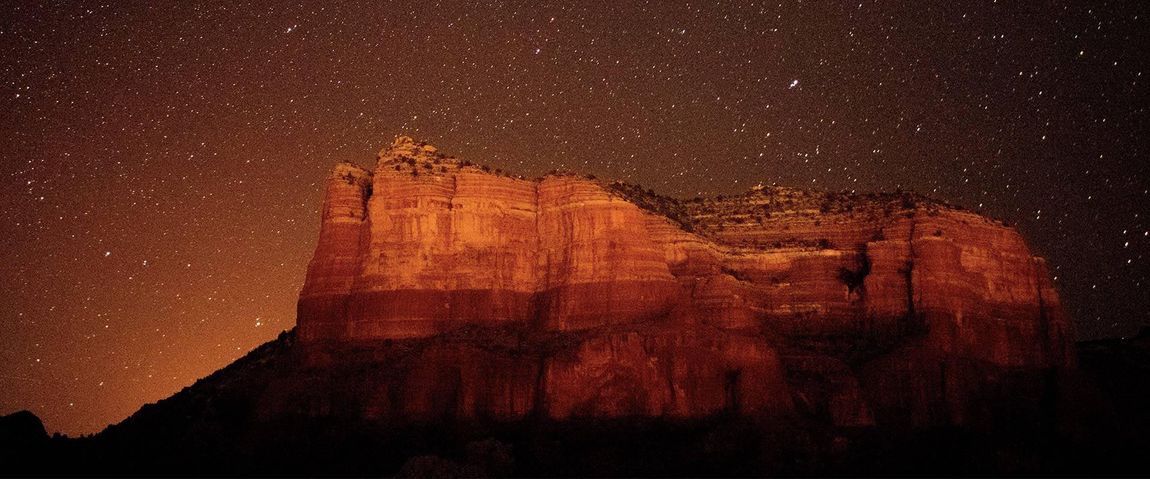 Red rock formation under a starry night sky.