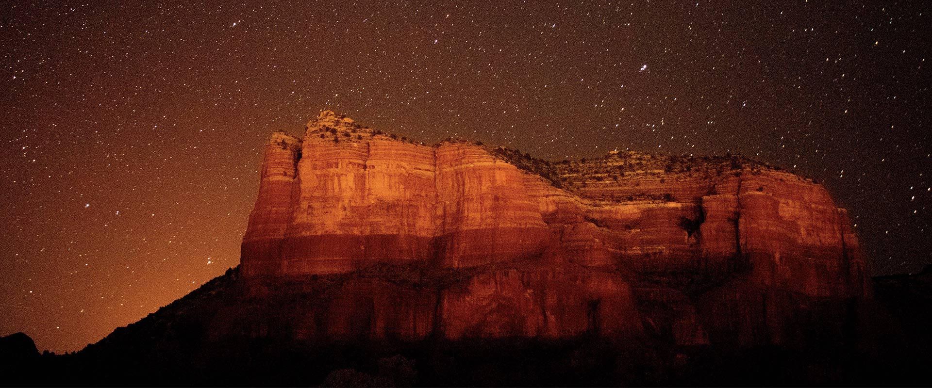 Red rock formation under a starry night sky.