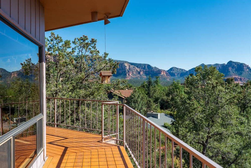 Balcony overlooking red rock mountains and green trees on a sunny day.