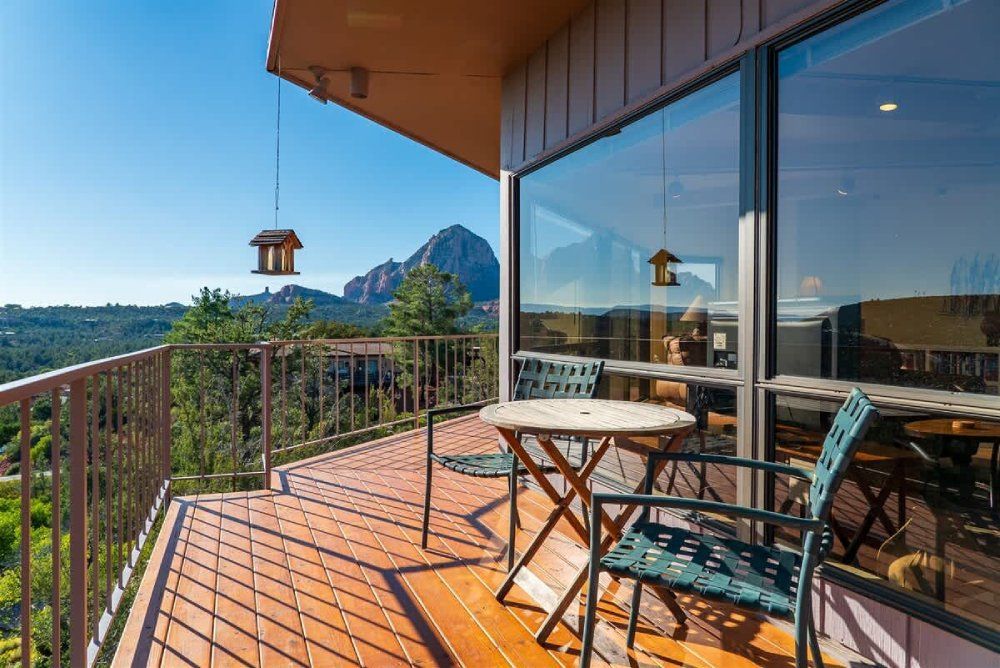 Balcony with a table and chairs, overlooking a mountain and trees on a sunny day.
