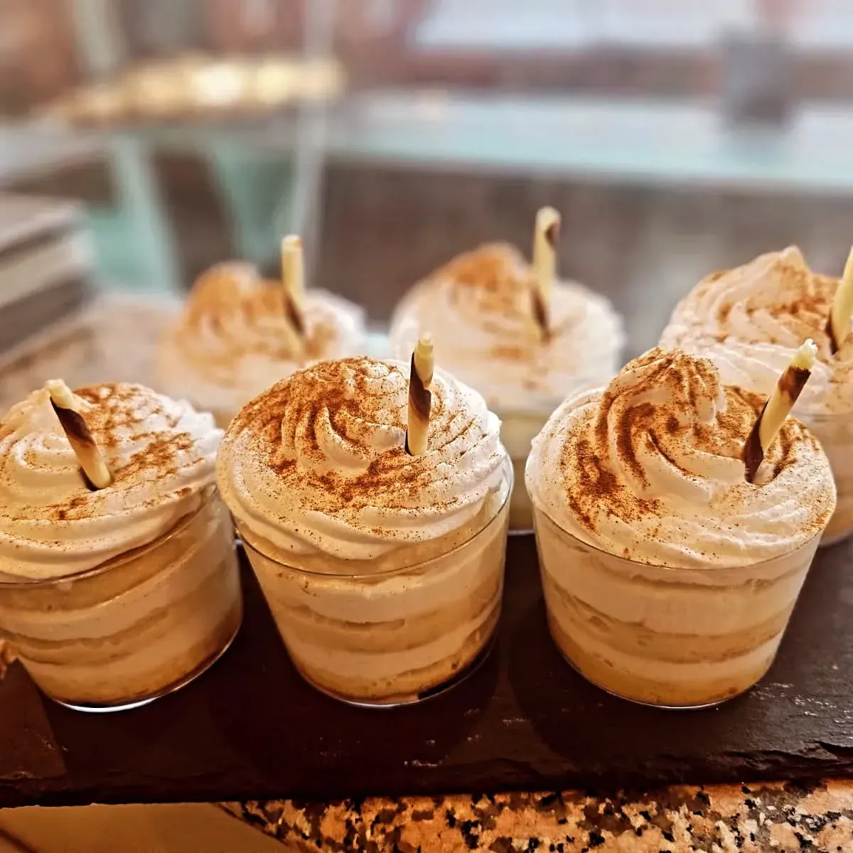 Una fila de cupcakes con crema batida encima están colocados sobre una mesa.
