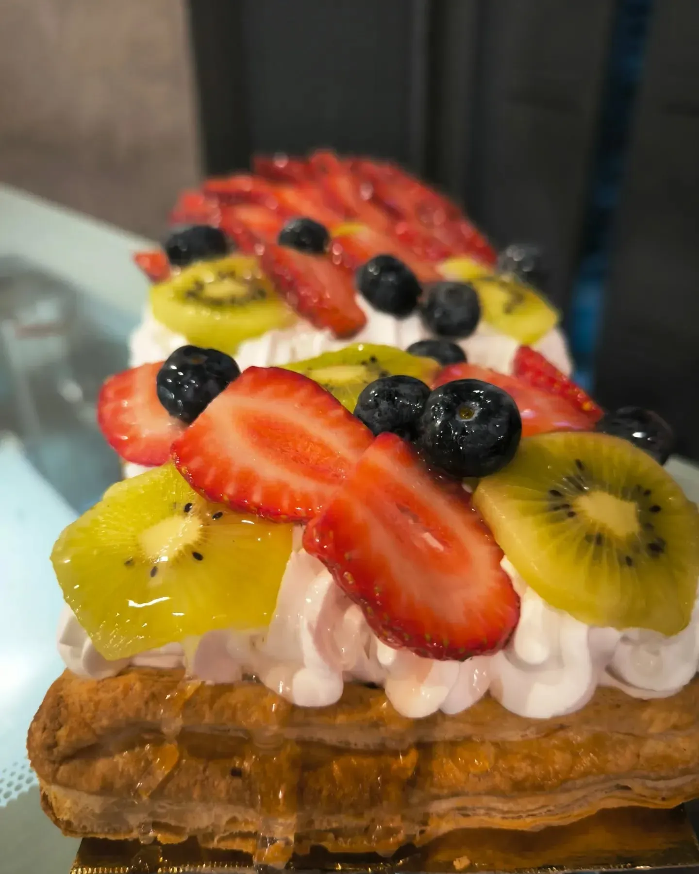 Un primer plano de un postre con fresas, kiwi, arándanos y crema batida.