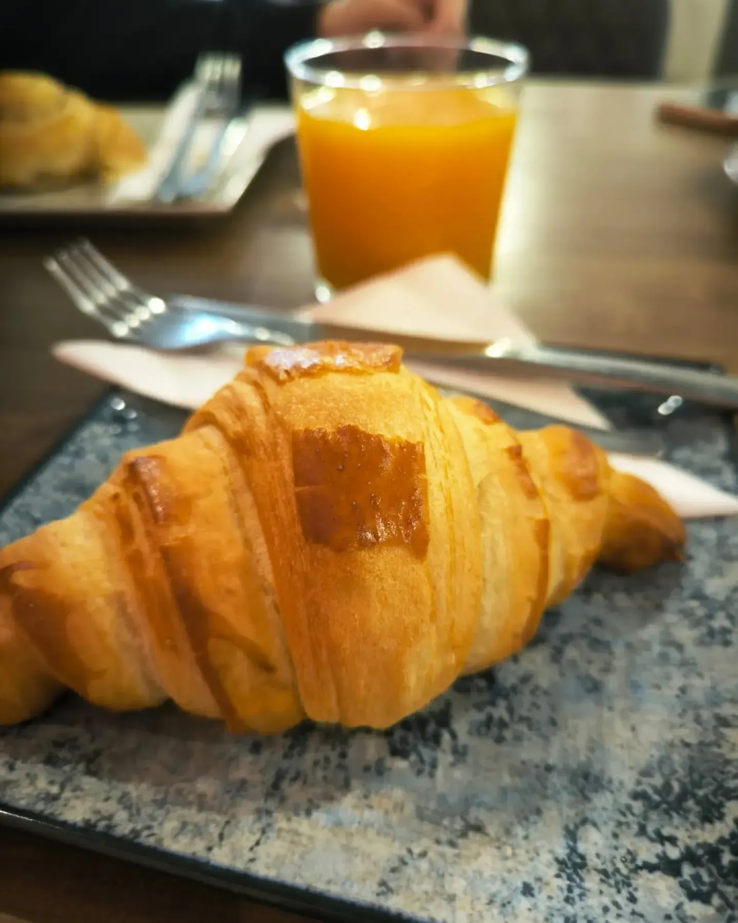 Un primer plano de un croissant en un plato con un vaso de jugo de naranja en el fondo.