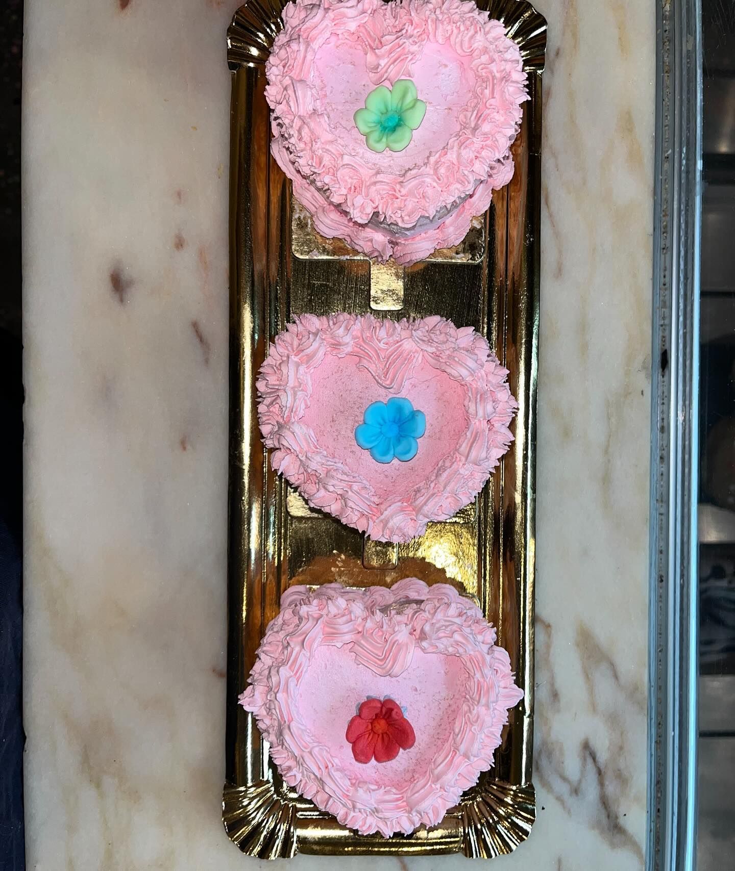 Tres cupcakes rosados en forma de corazón en una bandeja dorada