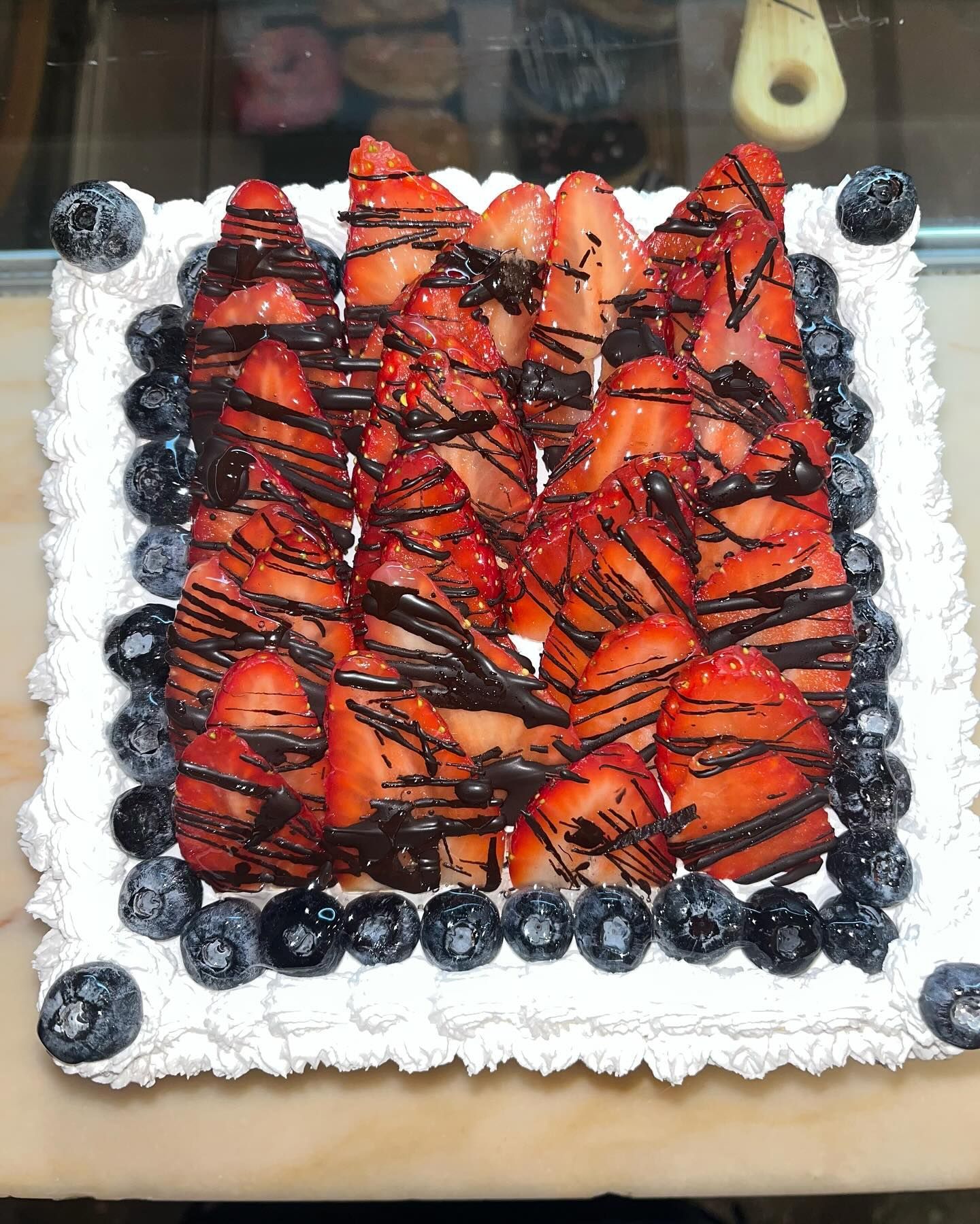 Un pastel cuadrado con fresas y arándanos encima.