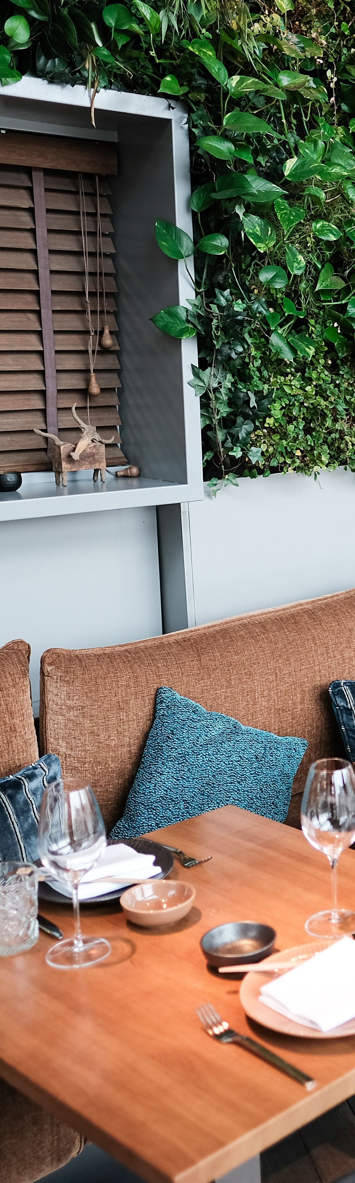 Espace repas avec table en bois, coussins d'assise tissés et verdure.
